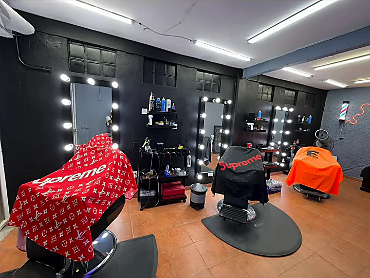 Interior de Black 98: muros negros, espejos rodeados de focos, sillones de barbero y piso de barro