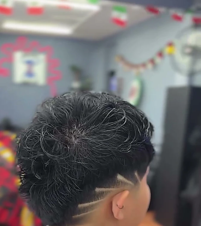 Cabello rizado arriba con degradado y dos rayas diagonales marcadas a navaja